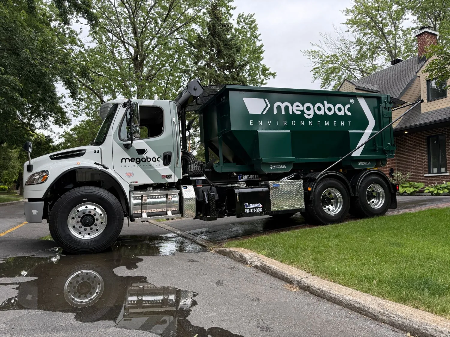 Megabac Environnement truck delivering a 20 cubic yard dumpster in a residential driveway in Boucherville