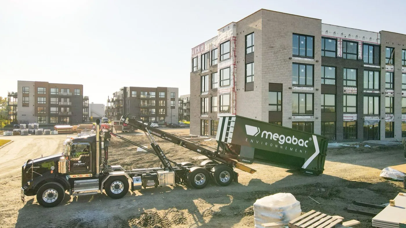 Megabac Environnement truck setting down a dumpster on a Greater Montreal job site