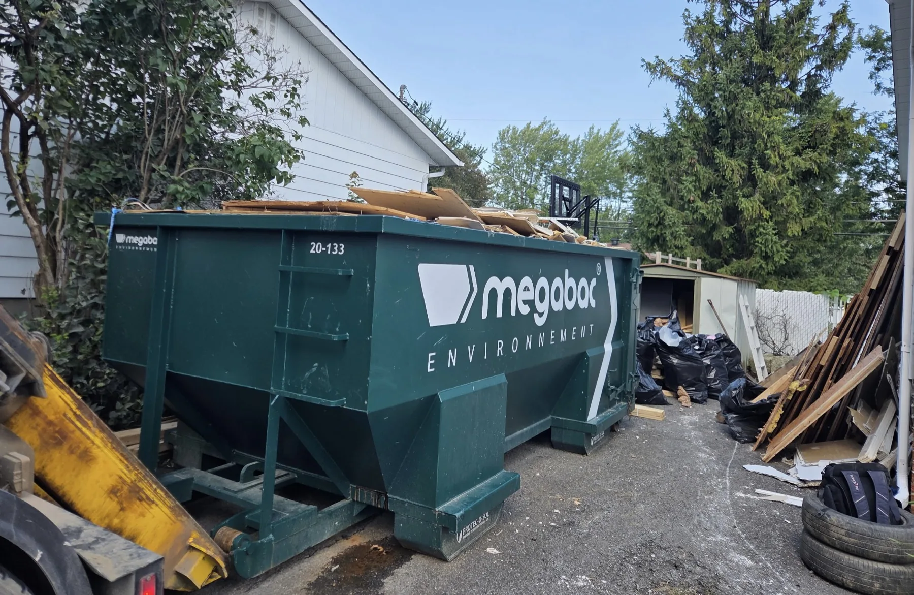 20 cubic yard Megabac dumpster filled with renovation materials in a residential driveway — wood, drywall and debris bags